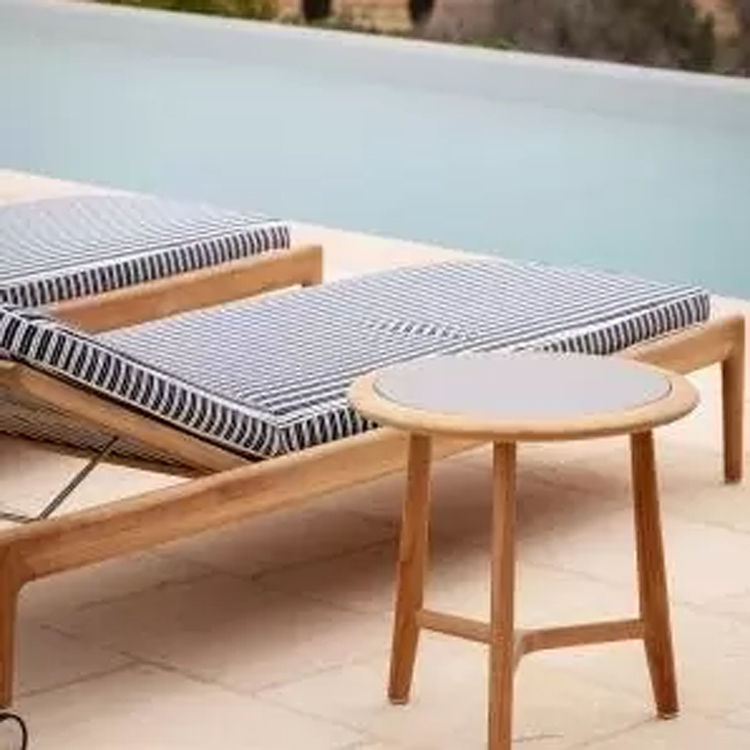 chaise longue en bois avec coussin rayé et table d'appoint en bois au bord d'une piscine sur un sol carrelé vue oblique | miniature