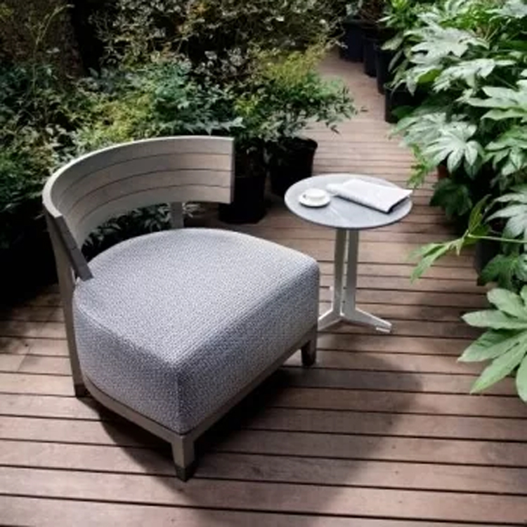 grijze loungestoel met tafeltje schuin bovenaanzicht op een houten platform tussen planten en bomen