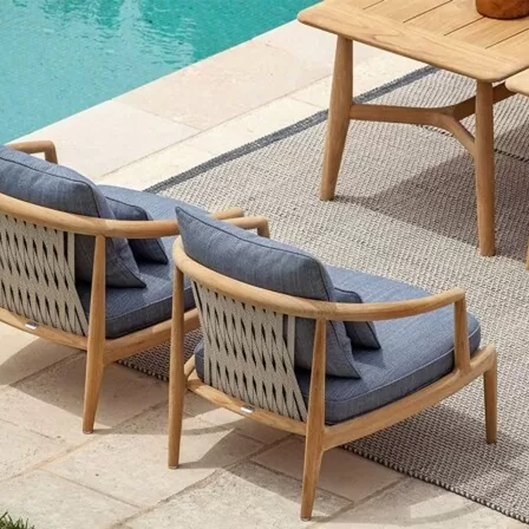 houten tuinset met blauw/grijze kussens op stenen tegelvloer langs zwembad schuin bovenaanzicht