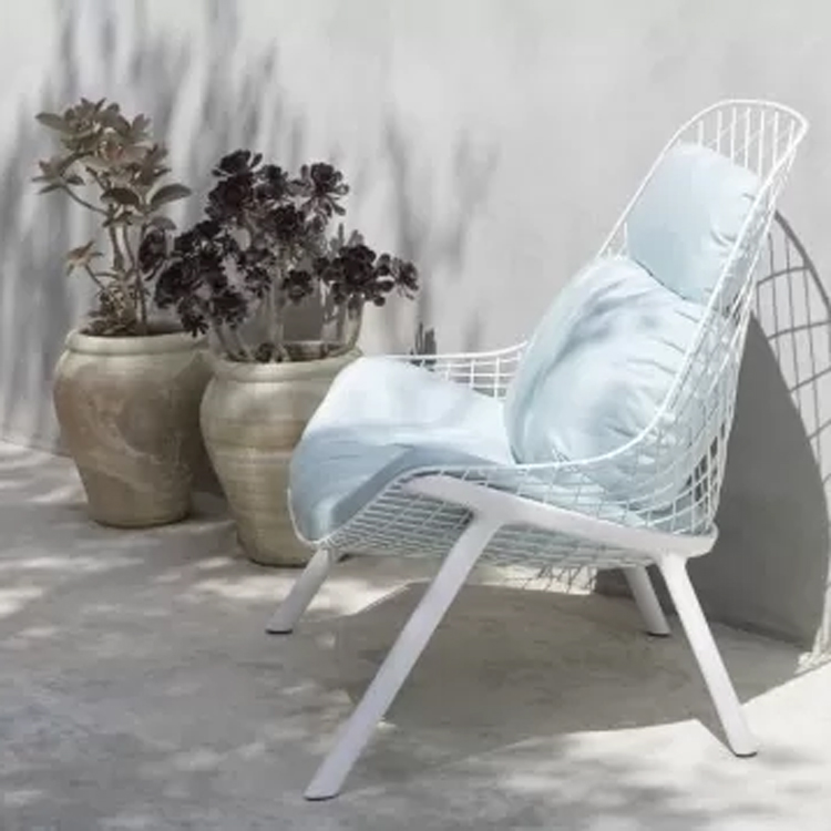 gran kobi witte tuinstoel lichtblauw kussen langs een grijze muur in de schaduw