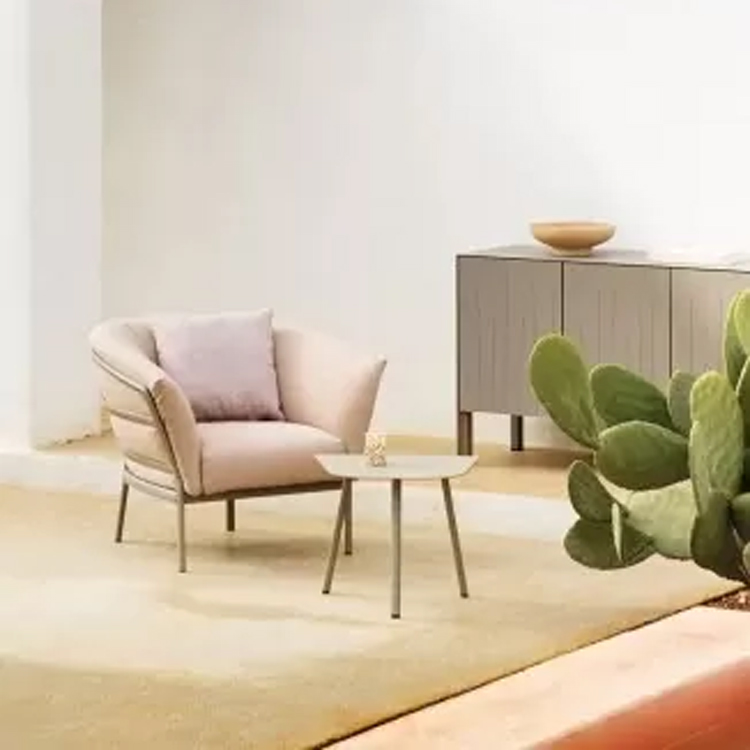 roze loungestoel met tafeltje binnen op een geel tapijt langs een grijze kast en witte muur